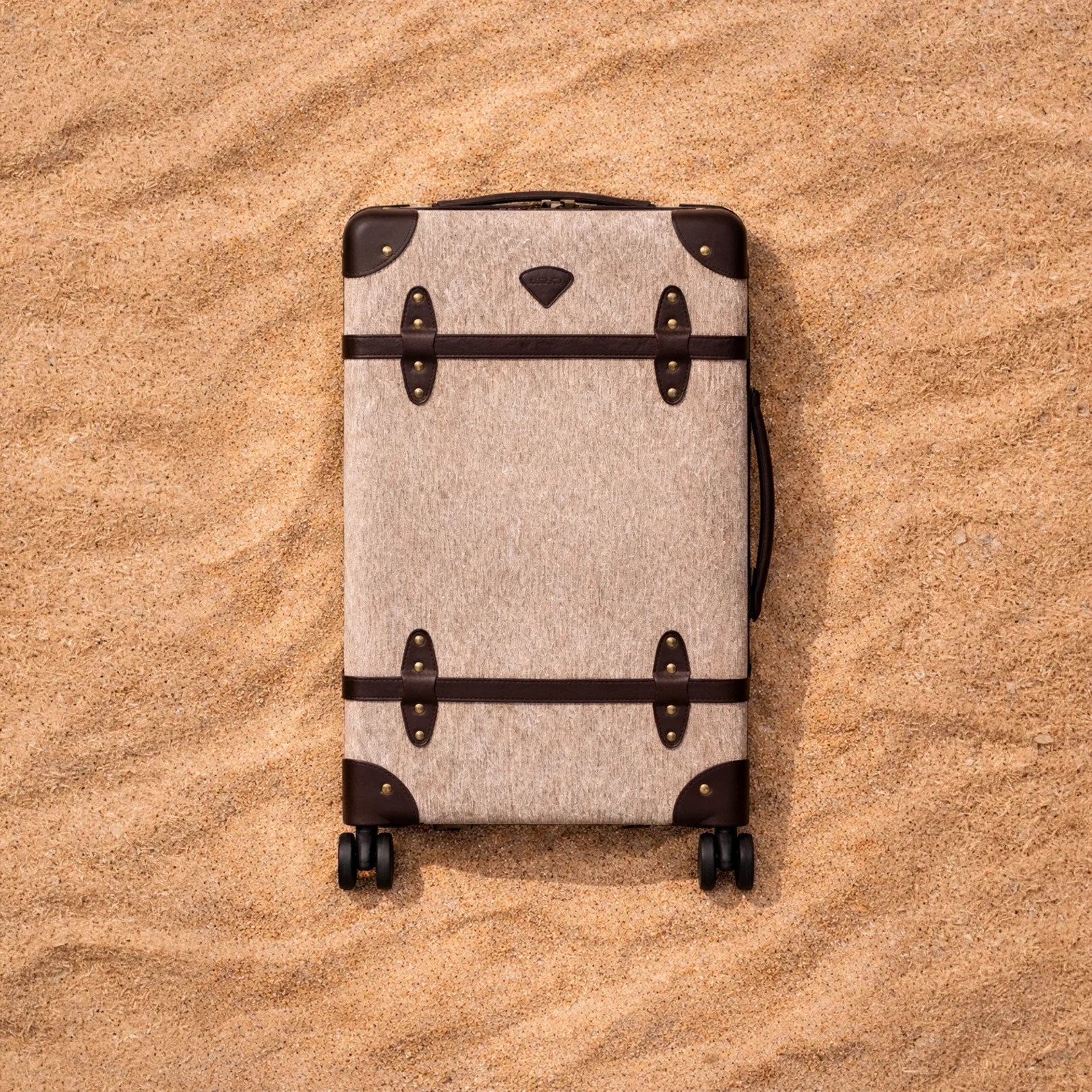Beige suitcase with black straps on a sandy surface